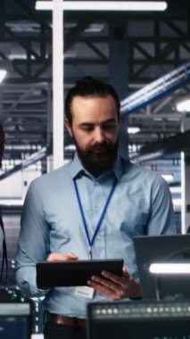 Sunucu odasındaki gülümseyen mühendislerin altyapı teşhislerini incelemek için yapay zekayı kullandıkları dikey video portresi. Veri merkezindeki neşeli bilişim çalışanları yapay zeka kullanarak performans verilerini analiz ediyorlar.