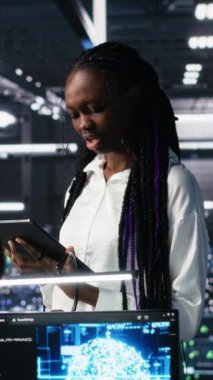 Veri merkezi geliştiricilerinden oluşan dikey video ekibi beyin fırtınası yapıyor, sinir ağı AI LLM 'yi izliyor. Yüksek teknoloji tesisinde çalışan takım arkadaşları sunucuların makine öğrenme süreçlerini denetliyor