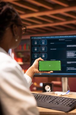 Masada oturan kadın AI LLM bot uygulaması ve modern şehir merkezindeki kapalı devre telefon kullanıyor. Afrikalı Amerikalı kişi bilgisayar ve akıllı telefon üzerinde büyük bir dil modeli programı kullanıyor