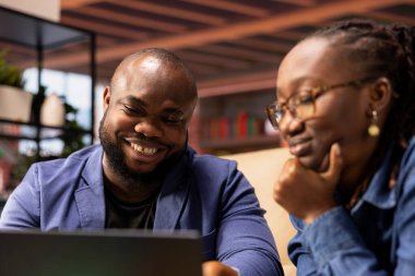 Oturma alanlarında yaşayan genç yetişkinler dizüstü bilgisayarlarında web sayfalarını karıştırırken kanepede oturup eğleniyorlar ve aletleriyle boş zamanlarının tadını çıkarıyorlar. Rahat, şık bir daire..