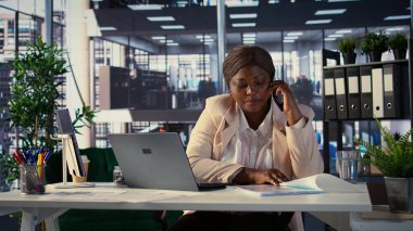 Afrika kökenli Amerikalı genel müdür performans ölçümlerini tartışmak ve iş geliştirme projesine odaklanmak için akıllı telefon çağrılarına cevap veriyor. Direktör, günlük işlemleri ve analizleri yapıyor. Kamera B.