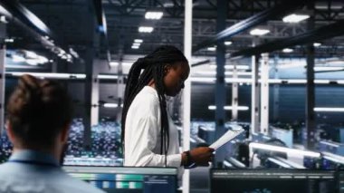 Veri Merkezi Mühendisleri, AI sistemlerini yönetiyor, zaman ve verimlilik için, evrak dosyalarına bakıyorlar. Afrika kökenli Amerikalı kadın ve Asyalı adam çok ırklı sunucu merkezinde doküman okuyorlar, kamera A