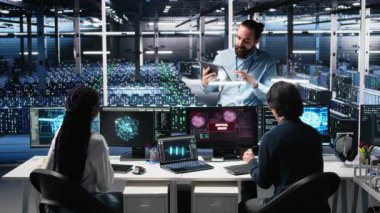 Veri Merkezi Yöneticisi, Yapay Zeka kullanırken kritik hatayı düzelten programcıları koordine ediyor. Sunucu odası lideri, yapay zeka ve kamera A 'yı kullanarak arızalı açılır pencereyi tamir eden işçilere nezaret ediyor.