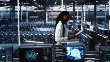 Veri Merkezi Mühendisleri, AI sistemlerini yönetiyor, zaman ve verimlilik için, evrak dosyalarına bakıyorlar. Afrika kökenli Amerikalı kadın ve Asyalı adam çok ırklı sunucu merkezinde doküman okuyorlar, kamera A