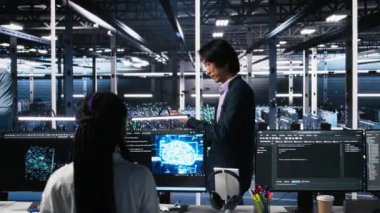 Veri Merkezi Yöneticisi, AI LLM 'leri izlemek için aygıt kullanan geliştiriciyi denetliyor. Ekip lideri, sunucuları denetleyen, makine öğrenme süreçlerini çalıştıran, kamera A tarafından yapılan işlemi kontrol ediyor.