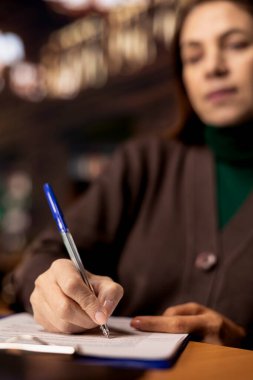 Olgun akademisyen kütüphanedeki dosyaların ders notlarını kopyalıyor, bir üniversite kampüsünde okuyor ve okuyor. Kadın, diploma tezinin hazırlanmasını araştırmayla sembolize ediyor. Kapat..