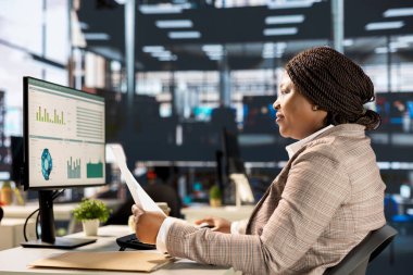 Odaklanmış Afro-Amerikan genel müdürü bilgisayar ve dokümanlardaki iş ve operasyonları çözmek için masa başında çoklu görev yapıyor. Stratejik kararlar verirken teslim tarihlerine yetişen kadın.