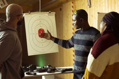Atış poligonu müşterileri birbirleriyle yarışıyor, hedefleri ateşli silahlarla vurduktan sonra elde edilen sonuçları karşılaştırıyorlar. Bir grup iş arkadaşı atış poligonu tesisinde ekip oluşturuyorlar. Silahlarla eğleniyorlar.