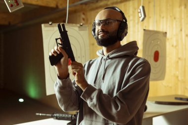Gülümseyen Arap atış poligonu müşterisi koruyucu gözlük takıyor güvenlik protokollerini takip ederek silah dolduruyor. Orta Doğulu mutlu bir adam silah dolduruyor ve düzenli güvenlik kurallarına göre silah taşıyor.