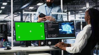Veri merkezinde yöneticiyle konuşan kadın programcı, yeşil ekranda yapay zeka tanılarını gözden geçiriyor. Bilişim uzmanı ve yönetici, yapay zeka sistemlerini A kamerası ve bilgisayar kullanarak optimize ediyor.