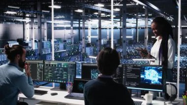 Veri merkezi geliştiricilerinden oluşan bir ekip beyin fırtınası yapıyor, sinir ağı AI LLM 'yi izliyor. Yüksek teknoloji tesisinde çalışan takım arkadaşları sunuculara güç veren makine öğrenme süreçlerini denetliyor, kamera A