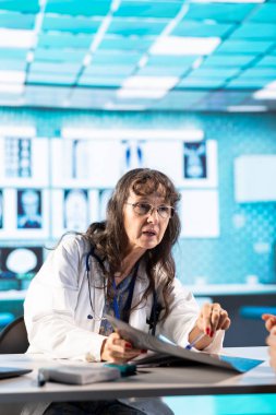 Kabinedeki hastaya teşhis raporlarını değerlendiren yaşlı bir kadın doktor. Profesyonel muayeneden sonra röntgen tarama sonuçlarını inceliyor. Pratisyen hekimden profesyonel tavsiye.