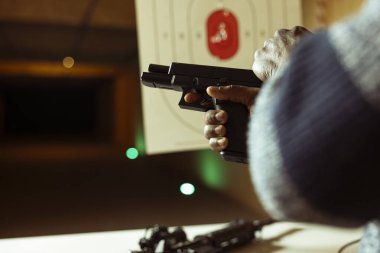 Kapalı alanda atış talimi yapan, silah kuşanmış, ateş etmek için mekanizma kuran bir müşteri. Alıştırma sırasında çekiç çeken kişinin yakın plan çekimi. Ateş etmeye hazırlanıyor.