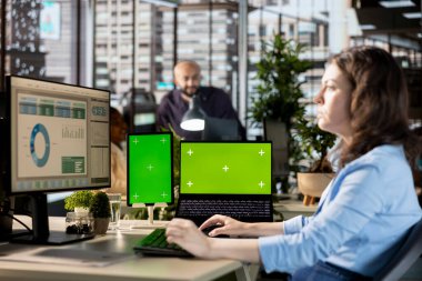 Genç yönetici, projenin geliştirilmesi için kurumsal çözümler üzerinde çalışarak masadaki izole görüntülerin yanında bilgi grafikleriyle çalışıyor. Analist çalışma istasyonunda çevrimiçi verileri gözden geçiriyor.