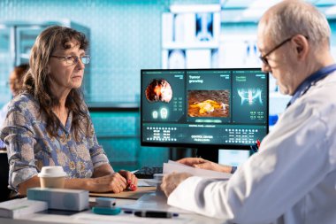 Kıdemli pratisyen ve hasta muayene sırasında hastane kayıtlarını inceleyip röntgen sonuçlarının bir taramasını yapıyorlar. Sağlık hizmetlerini sigorta konusunda vurgulayan hekim.