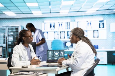 Bir hastayla tıbbi verileri inceleyen kadın pratisyen, sağlığa odaklı uzman istişare sırasında etkileşimi ve güveni teşvik eden. Afrikalı Amerikalı kız tavsiye istiyor..