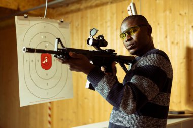 Tüfek tutan adamın portresi atış poligonunda eğlenceli bir atış deneyimi yaşıyor. Koruyucu ekipman takan kişi yarı otomatik silahla güvenli ve misafirperver bir ortamda pratik yapıyor.