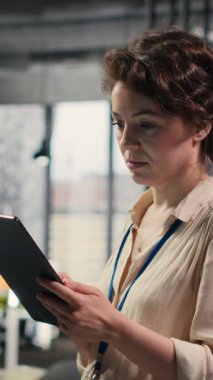 Dikey Video Kadını iş danışmanı, çalışma verimliliği için etkili yönetim ve stratejik planlama becerileri gösteren aylık raporlar oluşturmak üzere tablet üzerindeki grafikleri ve simgeleri inceliyor. Kamera B