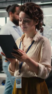 Yeni bir vizyon oluşturmak için dijital araçlar kullanan, modern ofis ortamında hedeflere ulaşmak için tablet üzerindeki performans veri içgörülerini gözden geçiren Dikey Video Kadın ofis yöneticisi