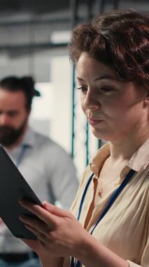 Yeni bir vizyon oluşturmak için dijital araçlar kullanan, modern ofis ortamında hedeflere ulaşmak için tablet üzerindeki performans veri içgörülerini gözden geçiren Dikey Video Kadın ofis yöneticisi