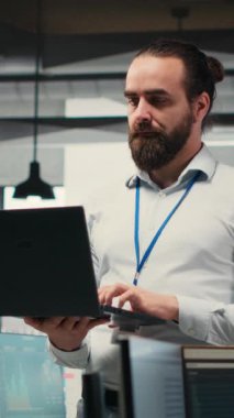 Dikey Video Erkek Patronu, iş arkadaşlarıyla çevrili modern bir işyerinde strateji kurarak, iş yönetimini geliştiren ayrıntılı raporlar ve açıklamalar oluşturmak için veri grafikleri ve grafikleri kullanır.