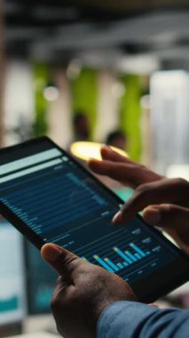 Siyahi çalışanın dikey videosu tablet üzerindeki çizelge analiz oturumuna katılıyor, iş stratejisini verimli proje yürütme hedefleriyle hizalamak için veri içgörülerini ve raporları koz olarak kullanıyor