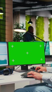 Dikey Video Çalışanı, ofiste yeşil ekranlı bir iş planlama ile meşgul, hedeflerle aynı hizayı sağlamak ve performans ölçümlerini optimize etmek için yazma rapor eder. Şirket tahminleri