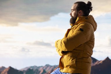 Kararlı dağcı dağların manzarasına hayran olmak için duraklıyor ve engin bir gökyüzü nefes kesici bir zemin oluşturuyor. Erkek yürüyüşçü doğa keşfi ve macerası için yürüyüş yapıyor..