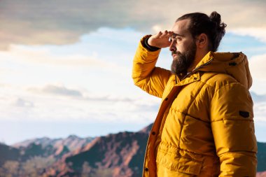 Genç maceraperest tepeden manzaralı bir dağ manzarasına bakarak doğanın yalnızlığını ve temiz havasını kucaklıyor. Farkındalık ve keşif hissi..