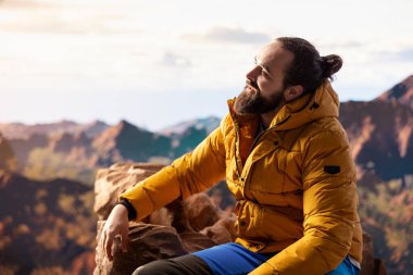 Genç maceracı dağın zirvesine ulaşıyor ve manzaraya hayran kalıyor, vadi manzarasını ve doğanın vahşi doğasını seviyor. Yürüyüşün ve gezinin tadını çıkaran bir yürüyüşçü..