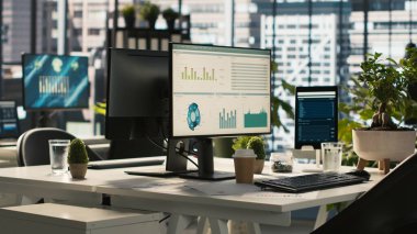 Modern ofis çalışma masasında bilgisayar monitörleri, grafikler ve veri analizleriyle çevrili, bitkiler ve şehir çevresi ile ilgili evraklarla çevrili, el kamerası görüntüleri