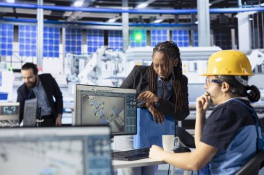 Fotovoltaik fabrikası çalışanı güneş pilleri tasarımlarını müdüre sunuyor. Güneş panelleri fabrika teknisyeni CAD programında bilgisayar simülasyonları yapıyor, Afrikalı Amerikalı denetçiyi bilgilendiriyor.