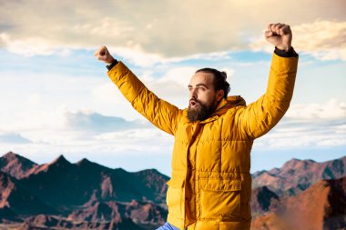 Tatmin olmuş maceracı, yüksek bir dağın tepesinde durur destansı manzarayı seyreder ve yürüyüş başarısıyla gurur duyar. Güçlü neşeli yürüyüşçü, tatminkar deneyimi hissediyor.