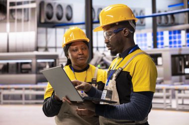 Endüstri 4.0 uzmanları akıllı üretim fabrikasındaki robot kol üretim hattını denetleyerek kusursuz otomasyonu sağlıyorlar. Siyah mühendisler otomatikleştirilmiş fabrikada dizüstü bilgisayarla dijital optimizasyon yapıyorlar..