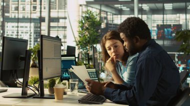 Ofis müdürünün yanında muhasebeci mali durumları kontrol ediyor, raporlar hazırlıyor. Takım lideri ve adam birlikte çalışıyor. Evrak dosyaları ve kamera B 'deki verileri karşılaştırıyorlar.