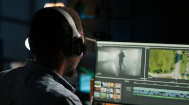 Siyahi adam video editörü yaratıcı içerik için çift monitörlerle çalışıyor, video görüntülerini düzenliyor ve medya yaratımı için renk değerlendirmesi yapıyor. Prodüksiyon sonrası erkek profesyonel işler. Kamera B.