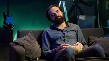 Yorgun adam gece geç saatlerde TV 'de program izliyor ve patlamış mısır yiyor, ekrana dikkatle bakıyor. Bütün gün pijamayla oturan yorgun bir adam, akılsız eğlence ve kamera A 'yı yiyor.