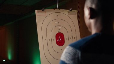 Atış poligonunda ateşli silah kullanan bir adam hareket halindeki hedefin sonuçlarına bakıyor. Rekabetçi atış sporu, keskinleştirme becerileri, hedef tahtası ve kamera A 'dan alınan denetim puanlarına yakın durun.