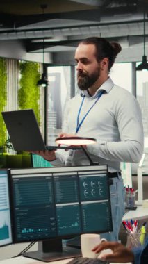 Dikey Video Erkek Takım Lideri, ortak çalışma alanındaki bir dizüstü bilgisayardaki analizleri izliyor ve iş verimliliği için günlük işleri yürütüyor. Geliştirme için performans ölçümleri ve diğer içgörüler kullanılıyor