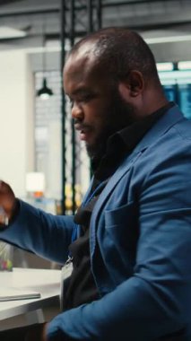 Dikey Video Siyah çalışanı notlarla yeni bir kalkınma stratejisi geliştiriyor, verileri analiz ediyor ve proje sonuçlarına çözümler üretiyor. Erkek profesyonel ofiste brifing raporları üzerinde çalışıyor.