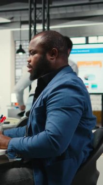 Dikey Video Siyah işadamı, yoğun çalışma nedeniyle sırt ve boyun ağrısına karşı, çalışma yerindeki kötü duruşunu düzeltiyor. Verimlilik ve verimlilik görevlerini çözen yönetici