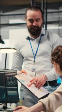 Aylık raporları tamamlamada birbirlerine danışan, iş verimliliğine ilişkin KPI veri içgörülerini gözden geçiren dikey video çok ırklı çalışma ekibi. Başarı için çalışanlar arası işbirliği. Kamera B.