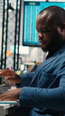 Modern çalışma alanındaki dikey Video Siyah Erkek Yöneticisi bir bilgisayar monitöründe öngörü ve iş stratejisini analiz ederek, üretkenlik için rapor yazmayı ve planlamayı güvence altına alır. Kamera B.