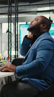 Dikey Afrikalı Amerikalı erkek, boyun tutulması ve sırt ağrısı ile kaslarını esnetiyor, kötü duruşunu düzeltiyor iş işlerinde çalışırken. Organizasyonun başarısına odaklan. Kamera A.