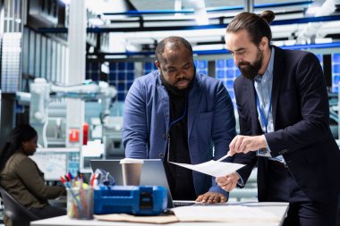 Profesyonel usta mühendisler kontrol panellerini inceliyor ve verileri analiz ediyor ve bir güneş enerjisi üretim tesisinde bilgi paylaşımı yapıyor. Teknik içgörü ve grup işbirliği.