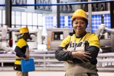 Endüstri 4.0 kadın mühendis akıllı üretim tesisinde duruyor. Siyah kadın, robot kolları, taşıma bantları ve otomatik sistemlerle endüstriyel otomasyon hatlarının sorunsuz çalışmasını sağlıyor..