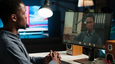 Afro-Amerikalı bir adam müdürle masa başında video konferansı yapmayı seviyor, iş arkadaşıyla internet üzerinden ofis kurulumunu kullanarak tartışmayı seviyor. Genç Ortaklar takım toplantısı online. Kamera B.