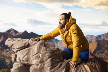 Genç maceracı dağın zirvesine ulaşıyor ve manzaraya hayran kalıyor, vadi manzarasını ve doğanın vahşi doğasını seviyor. Yürüyüşün ve gezinin tadını çıkaran bir yürüyüşçü..