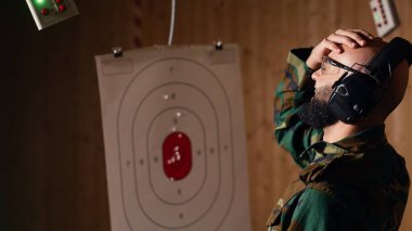 Atış poligonundaki adam, hedefi tabancayla vuruyor. Avuç içiyle vuruyor. Boğa güreşi yapamadığı için üzgün hisseden hayal kırıklığına uğramış kişi, kamera B