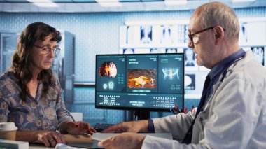 Genel pratisyen hekim termometrenin ateş ölçümlerini alıyor, kabinedeki yaşlı kadın hastaya danışıyor. Hastalık önleme sıcaklığını kontrol eden yaşlı bir doktor. Kamera A.